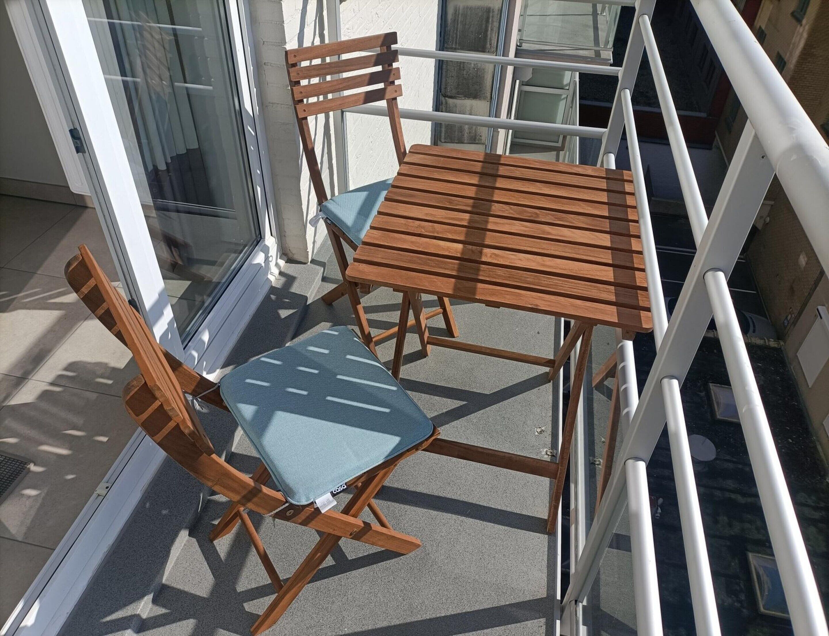 A balcony with a wooden table and chairs, a glass door, and a white railing.