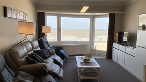 A living room with a sofa, a coffee table, a TV, and a view of the beach. - Apartment in Nieuwpoort by the Beach (Nieuwpoort)