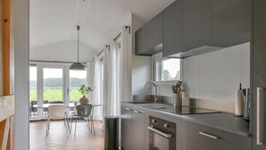 A modern kitchen with a large window, stainless steel appliances, and a dining area with a view of the outdoors. - Chalet in Dutch Park With Garden and Terrace (Hoogersmilde)