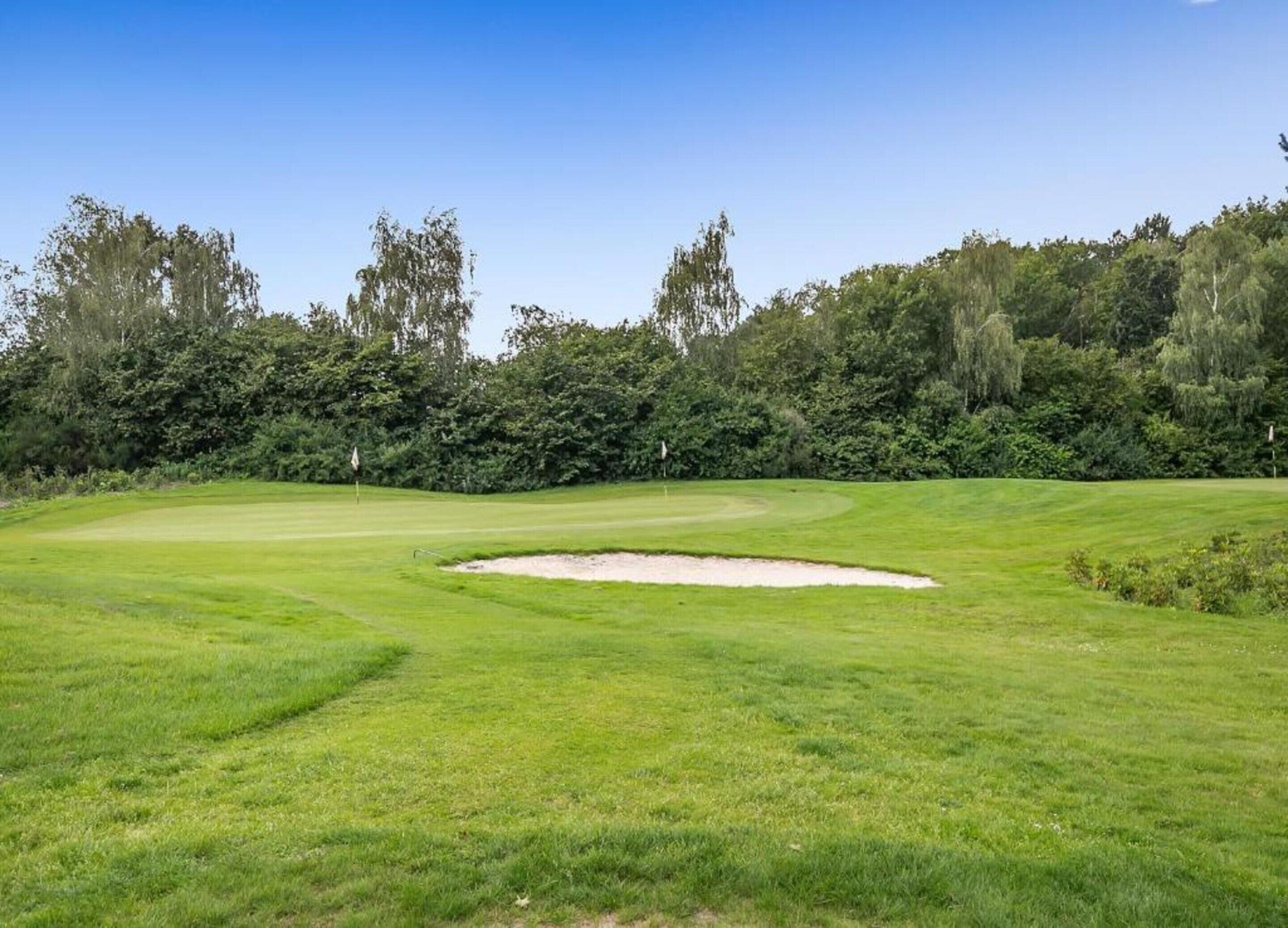 A golf course with a sand bunker, well-maintained grass, and a flag marking the hole.
