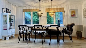 Un comedor con mesa y sillas, un mueble con puertas de vidrio y una ventana con vista a zonas verdes.
