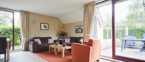 A spacious living room with a sofa, armchair, and coffee table, large sliding glass doors leading to a patio area.