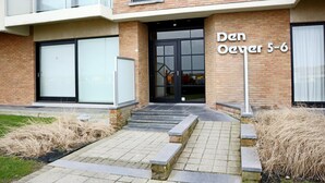 A modern building with a brick facade, a glass door entrance, and a sign reading "Den Oever 5-6". - Seaside Serenity Apartment (Nieuwpoort)