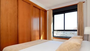 A hotel room with a large bed, wooden paneling on the walls, a window with a view of a cityscape, and a lamp on the nightstand. - Belvilla by OYO Apartment in Fuengirola (Fuengirola)