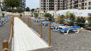 A beachside walkway with lounge chairs and umbrellas, surrounded by buildings with balconies. - Belvilla by OYO Apartment in Fuengirola (Fuengirola)