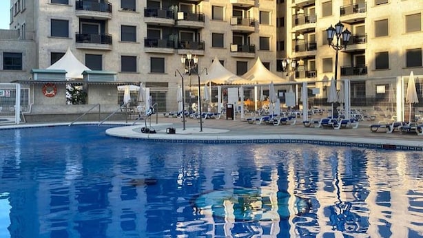 A swimming pool with lounge chairs and umbrellas, surrounded by a high-rise building with balconies. - Belvilla by OYO Apartment in Fuengirola (Fuengirola)