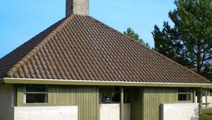 Un bâtiment avec un toit recouvert de tuiles, une cheminée et une porte verte.