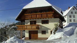 Eine zweistöckige Chalet mit Holzbalkon, schneebedecktem Dach und Holztür.