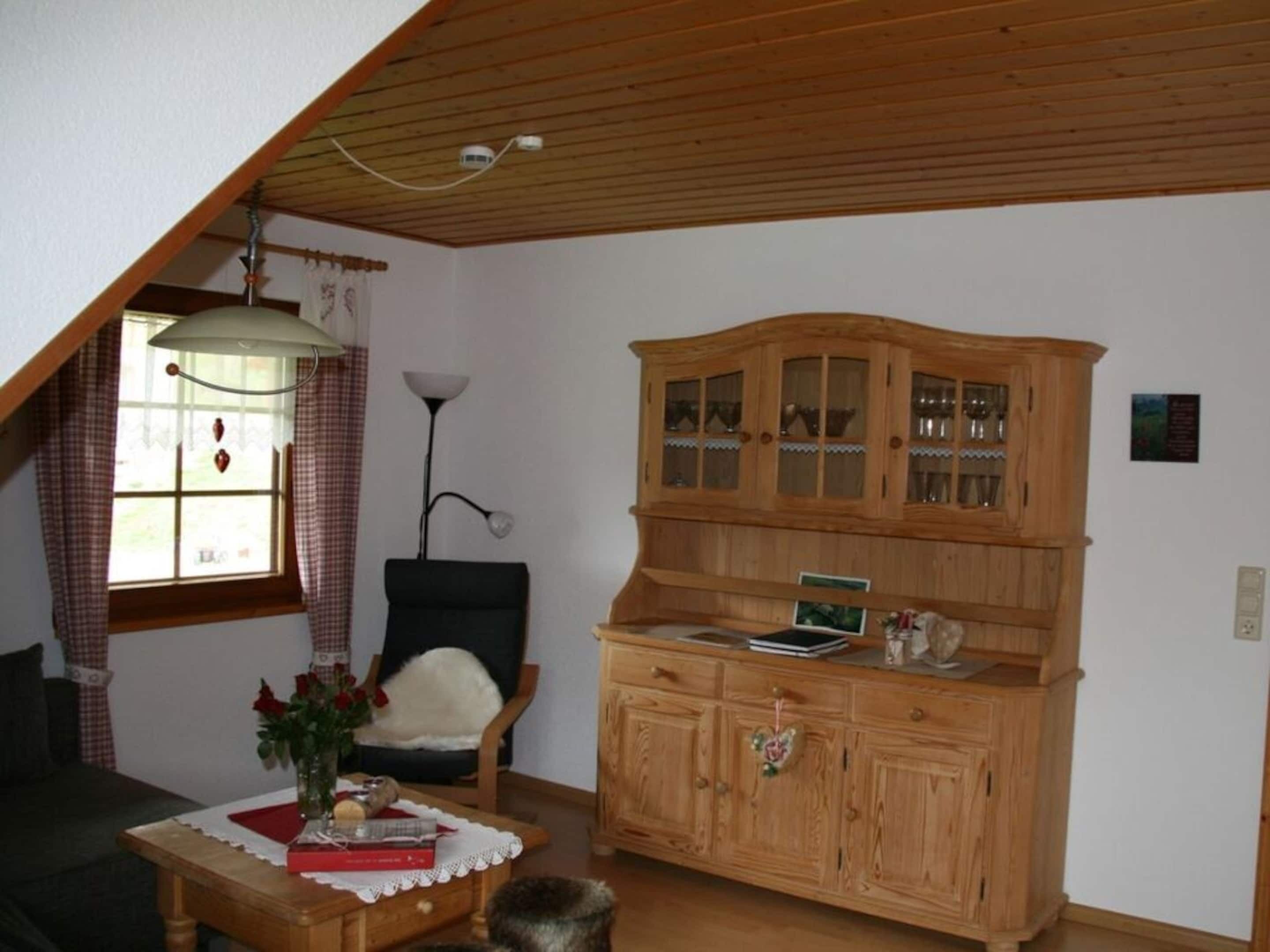 Een knus ingerichte kamer met een houten kast, een stoel, een tafel met een bloevas en een lamp.