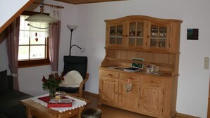 Ein gemütliches Zimmer mit einem Holzkasten, einem Sessel, einem Tisch mit Blumen und einer Lampe.