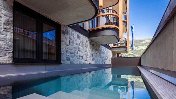 A modern pool area with a stone wall and a curved balcony. - Modern Holiday Apartment With Balcony (Fuegen)
