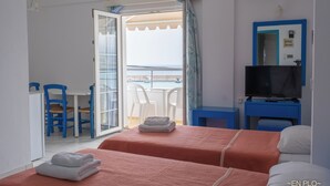 A hotel room with two beds, a TV, a balcony with a table and chairs, and a view of the sea. - Enplo Apartments (Hersonissos)