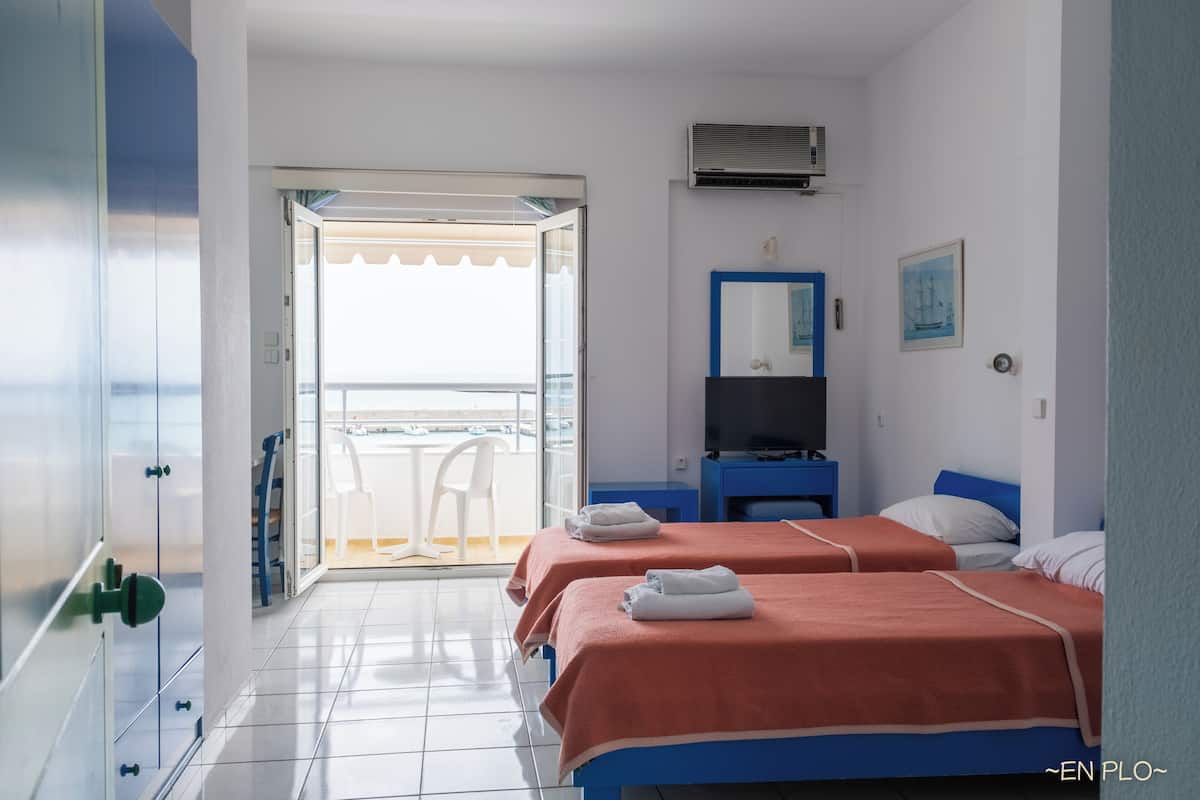 A hotel room with two beds, a TV, a mirror, and a balcony with a chair.
