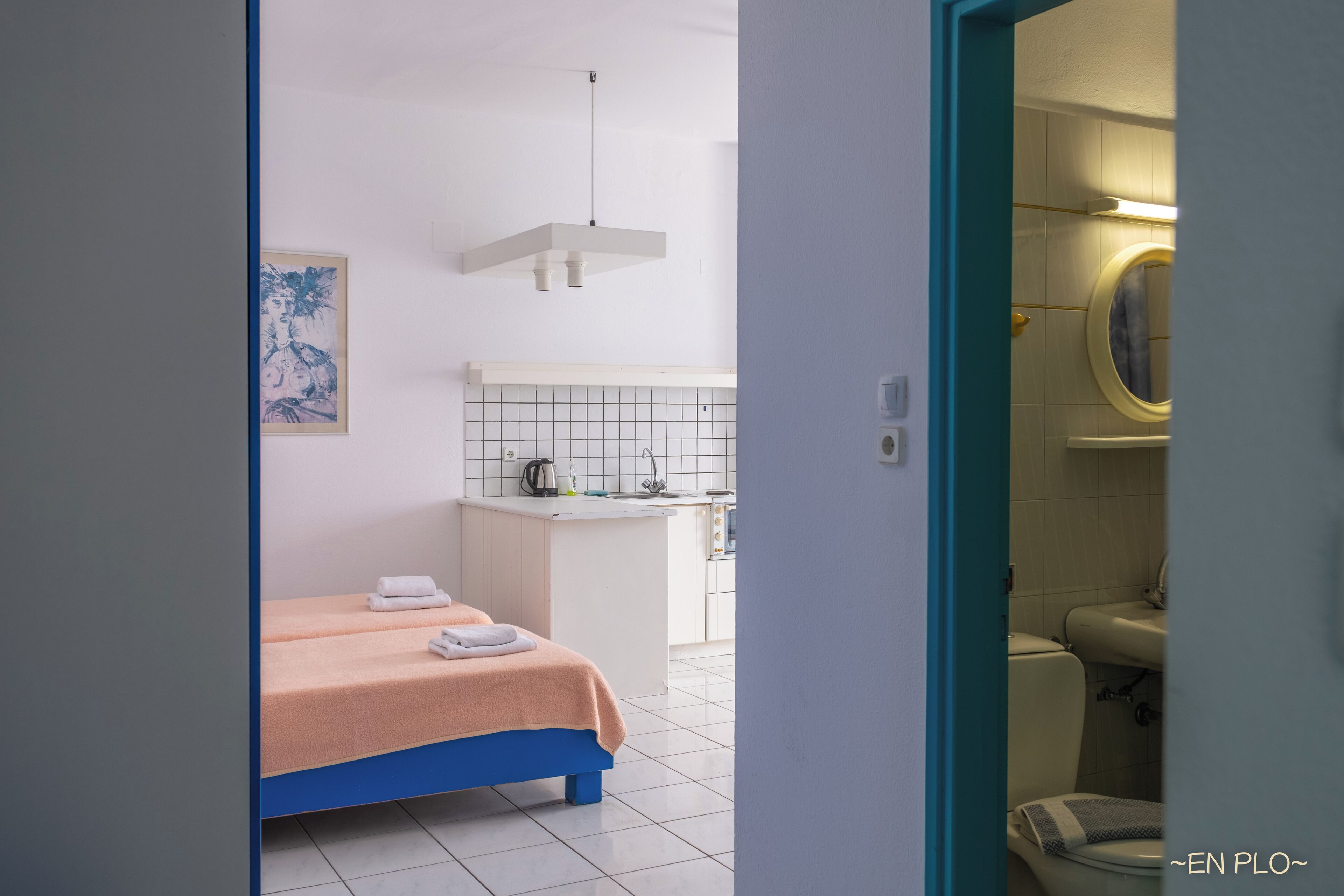 Ein Hotelzimmer mit Bett, einer kleinen Küchenzeile, einem Badezimmer mit Toilette und Waschbecken sowie einem Bild an der Wand.