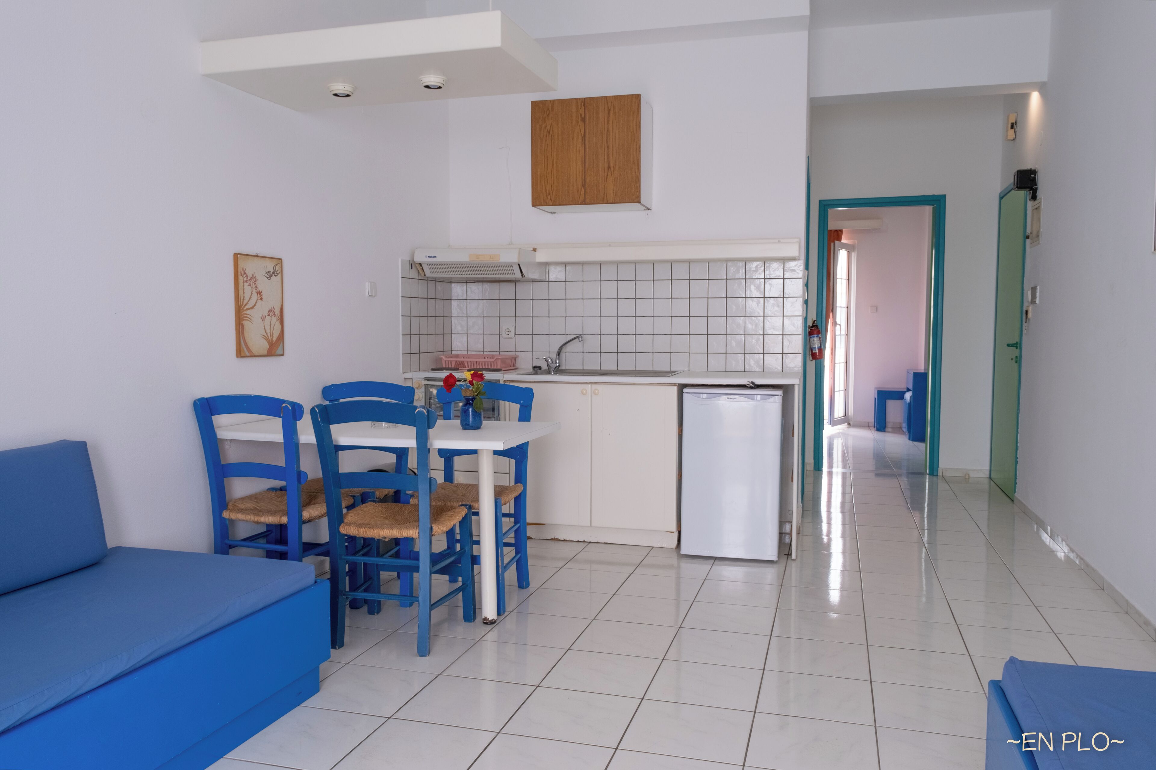 A compact kitchen with a dining area, white tiled backsplash, and a small refrigerator.
