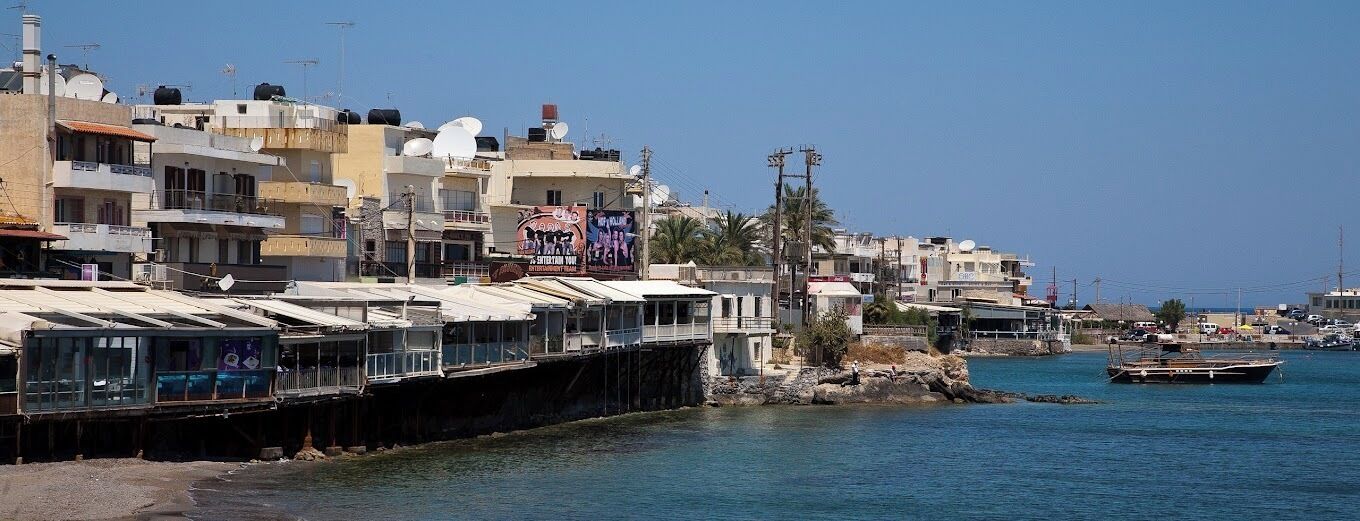 A coastal town with buildings along the waterfront, a pier extending into the water, and a boat docked nearby.