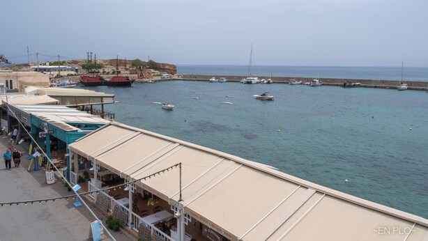 A coastal marina with boats docked, a sandy beach, and a building with a covered walkway. - Enplo Apartments (Hersonissos)