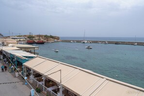 A coastal marina with boats docked, a sandy beach, and a building with a covered walkway. - Enplo Apartments (Hersonissos)