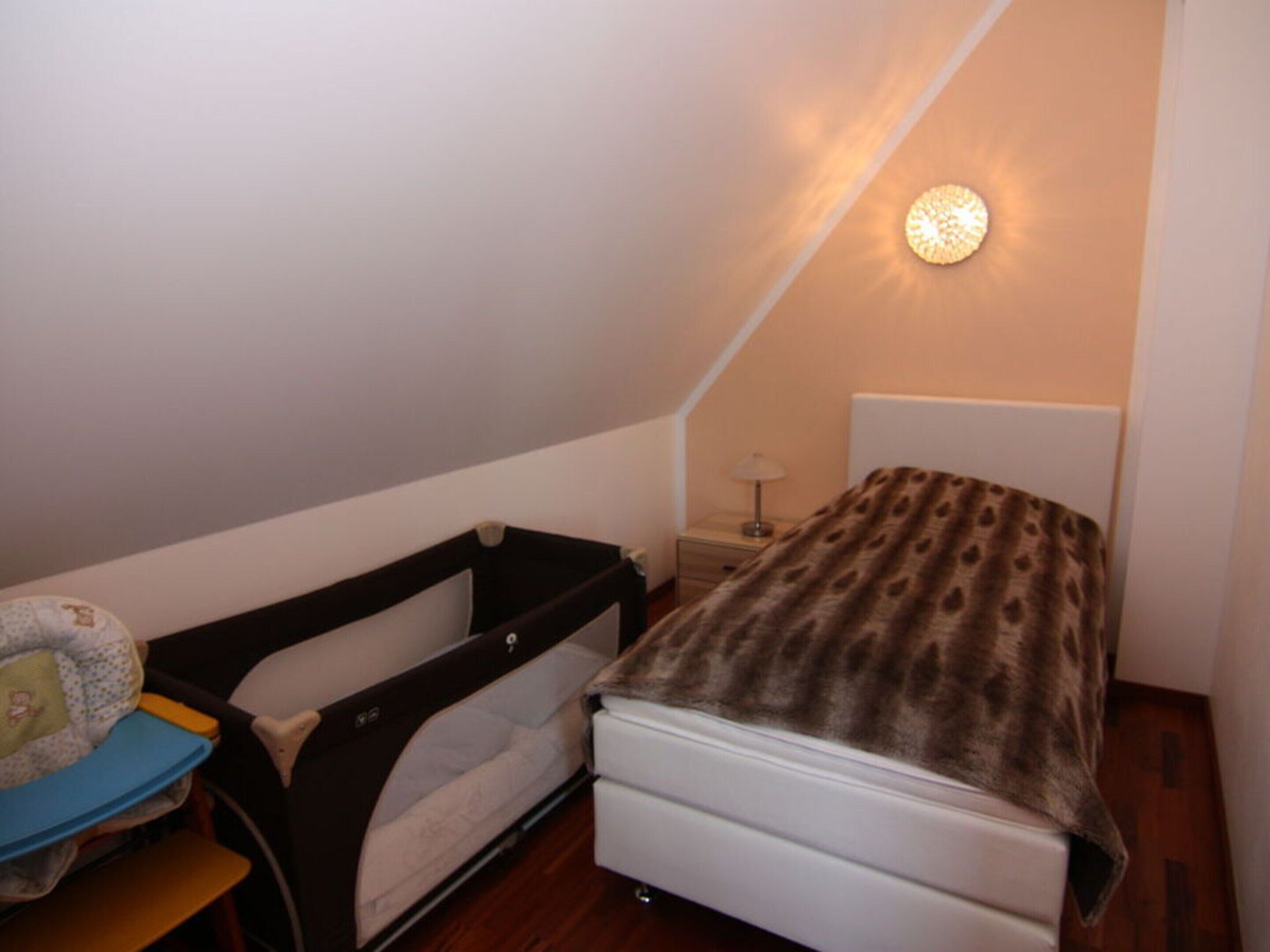 Una habitación pequeña y acogedora con una cama individual, una mesita de noche y una cuna para bebé.