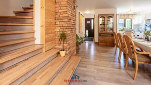 Un vaste espace de vie agrémenté d’un escalier en bois, d’un mur en briques, d’un coin repas avec des meubles en bois et d’une cuisine équipée de placards et d’une fenêtre.