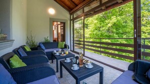 Une terrasse couverte, meublée de mobilier en osier, avec une table dressée pour le petit-déjeuner et une vue sur une végétation luxuriante.