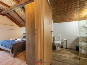 Quarto com guarda-roupa de madeira, cama com colcha azul e banheiro com vaso sanitário e box de vidro.
