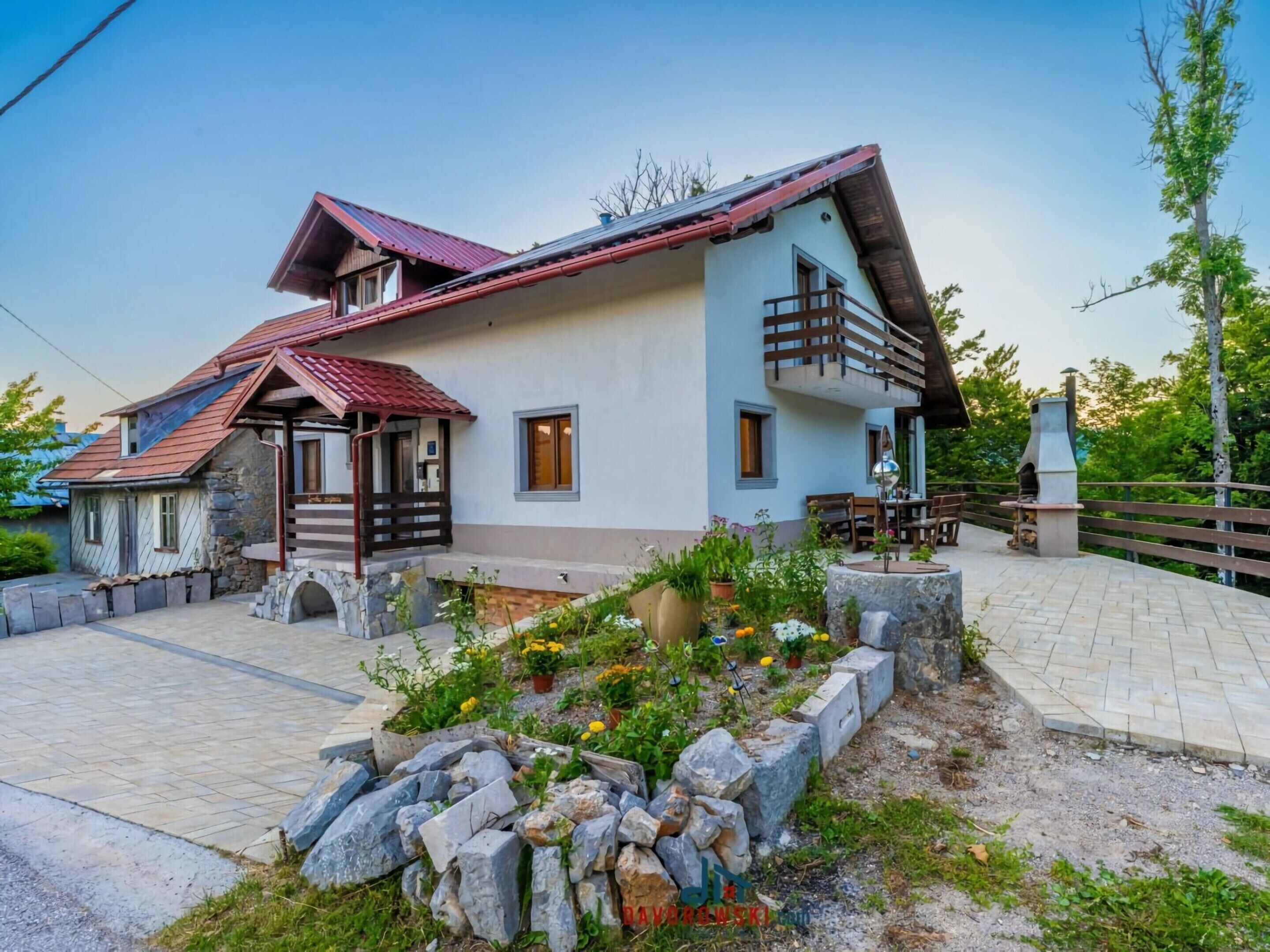 Una casa de dos pisos con base de piedra, techo rojo y un balcón.
