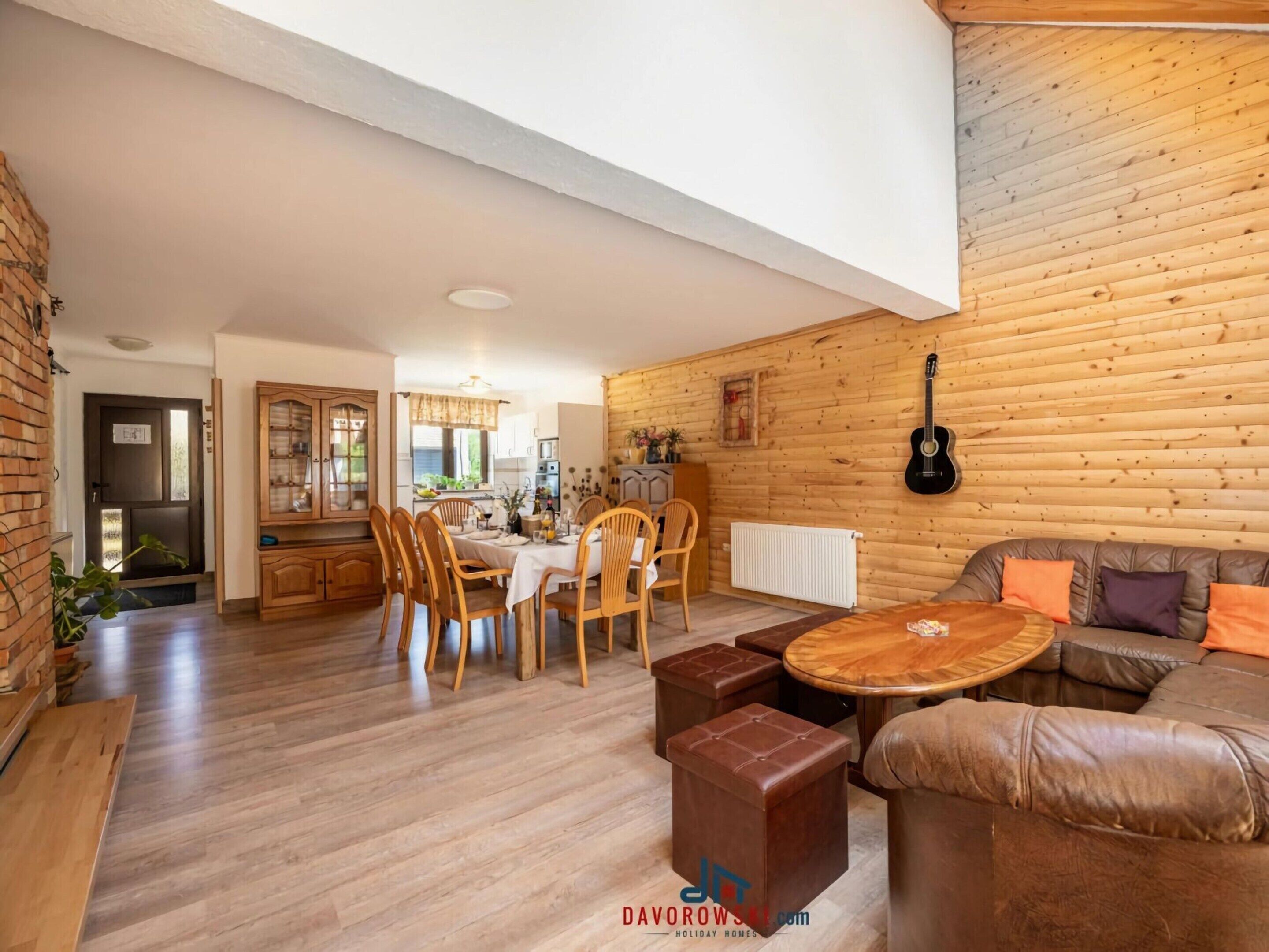Amplia sala de estar con una mesa de comedor de madera, sillas, un sofá de cuero y una pared de madera con una guitarra.