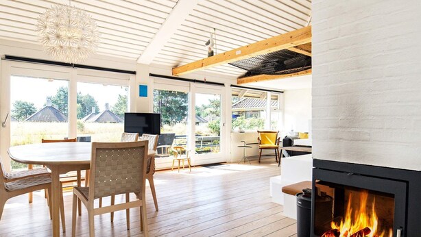 A modern living room with a fireplace, wooden flooring, and large windows offering a view of the outdoors. - Family Holiday Home in Karrebaeksminde (Karrebæksminde)
