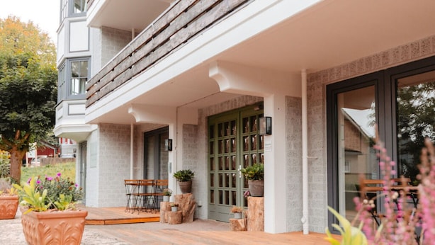 A modern building with a covered outdoor area featuring a wooden deck, outdoor seating, and potted plants. - Granetal.quartier-apartment Harzidylle (Goslar)
