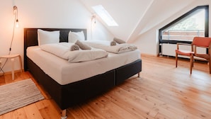 A modern bedroom with a large bed, a small stool, a chair, and a skylight. - Granetal.quartier-apartment Harzidylle (Goslar)