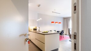 A modern kitchen with a central island, white cabinets, and a dining area with a red rug. - Apartment in St-idesbald Near the Beach (Koksijde)