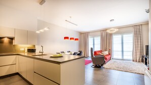 A modern kitchen with a central island, a dining area with a red chair, and a large window with curtains. - Apartment in St-idesbald Near the Beach (Koksijde)