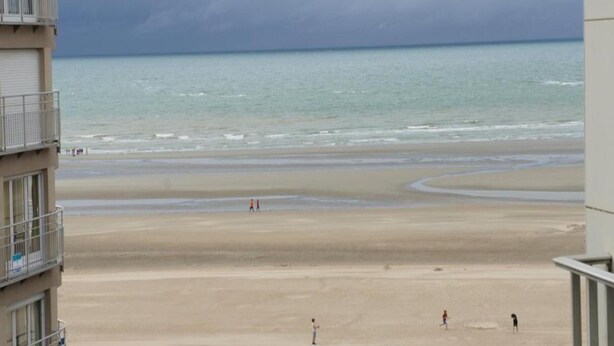 A beach view from a building with balconies overlooking a sandy beach and the sea under a cloudy sky. - Apartment in St-idesbald Near the Beach (Koksijde)