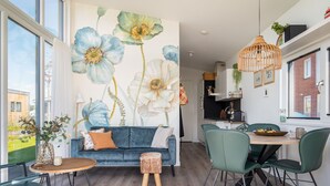 Un salon moderne avec un canapé bleu, une table à manger et des chaises, ainsi qu’une grande fresque florale sur le mur.