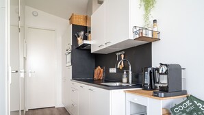 Une cuisine moderne avec des meubles blancs, un plan de travail noir, une machine à café et une plante suspendue.