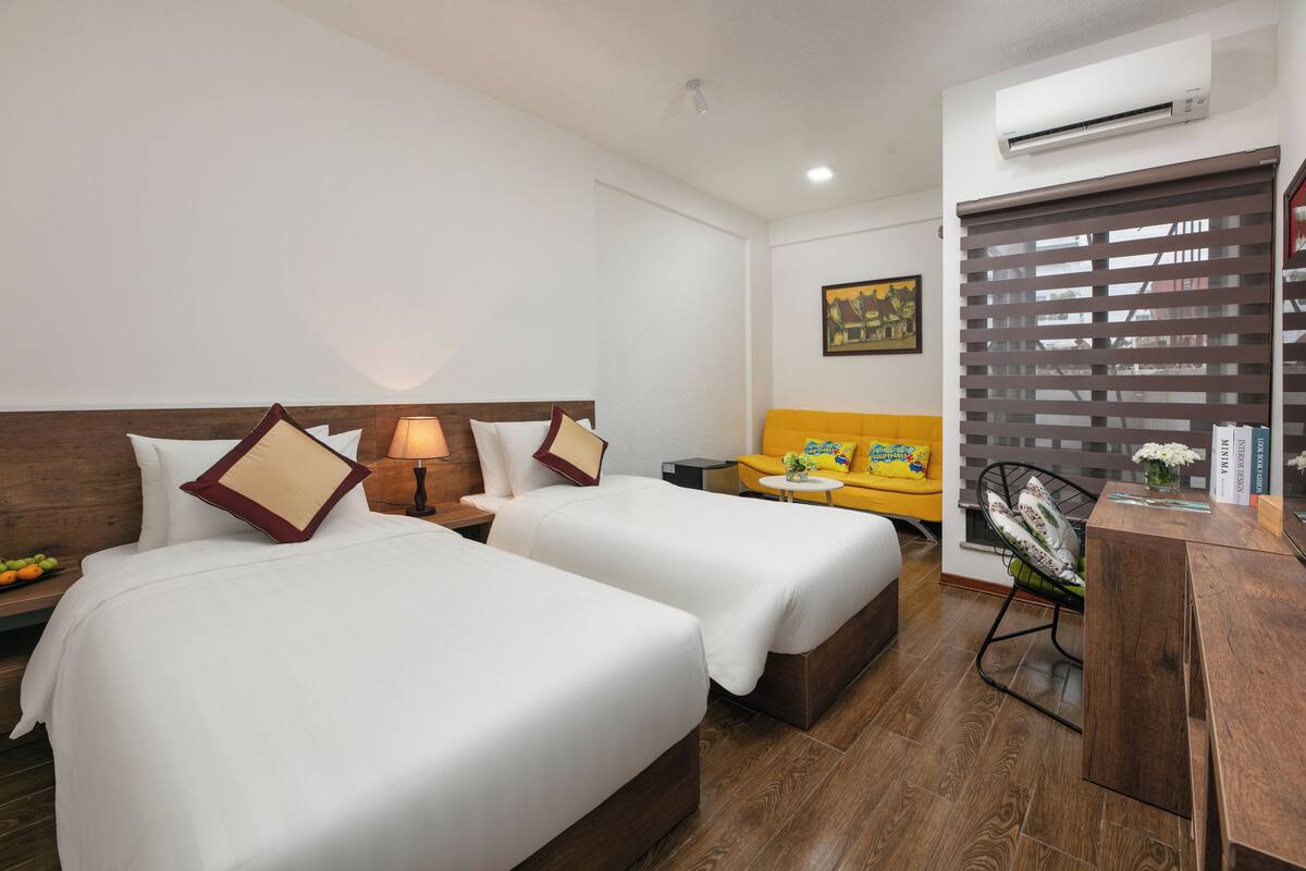 A hotel room with two beds, a sofa, a desk, and an air conditioning unit.