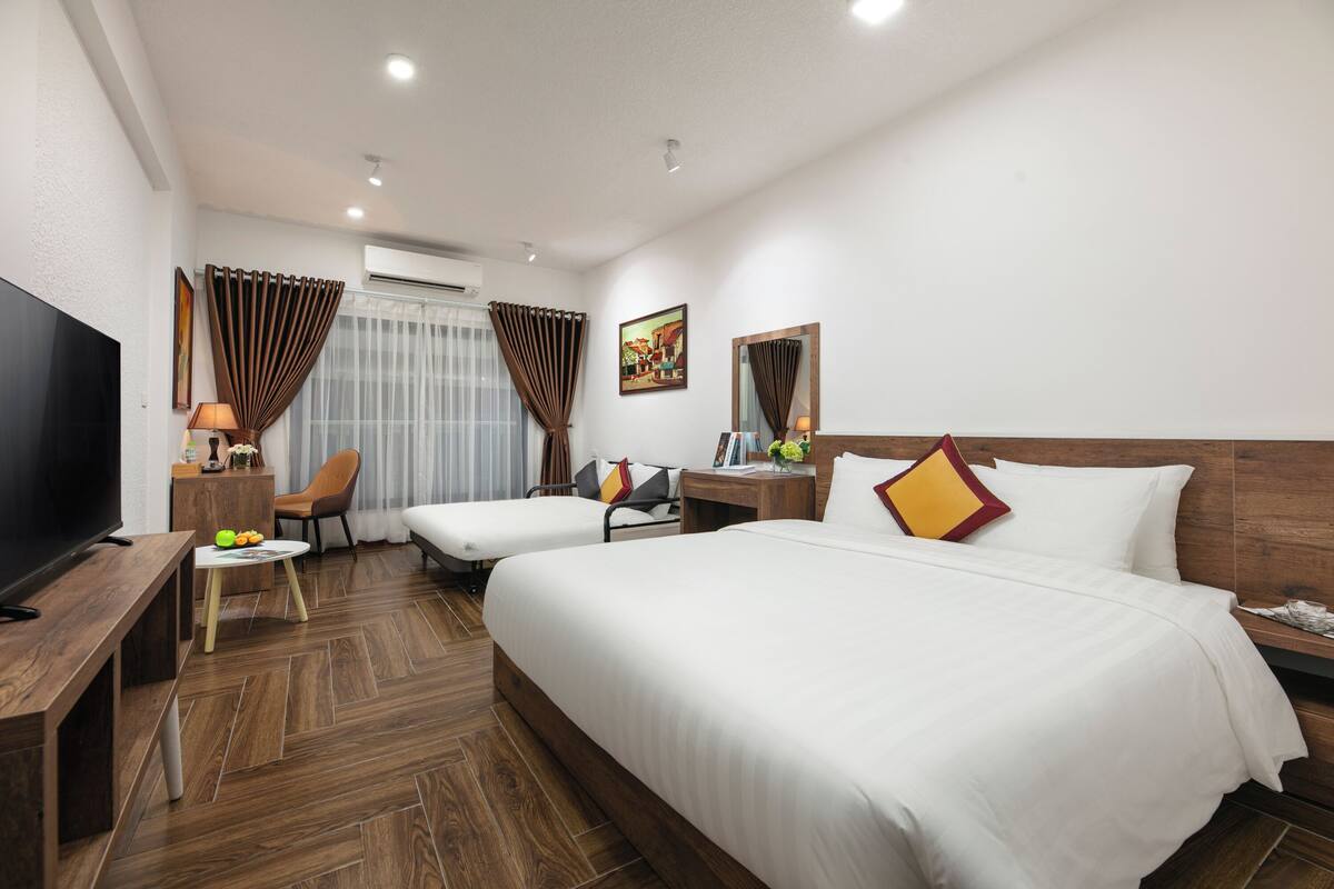 A hotel room with two beds, a TV, a desk with a lamp, and a chair.