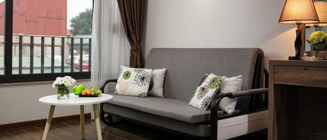 A modern living room with a grey sofa, a small round table with a vase of flowers, and a lamp on a wooden side table.