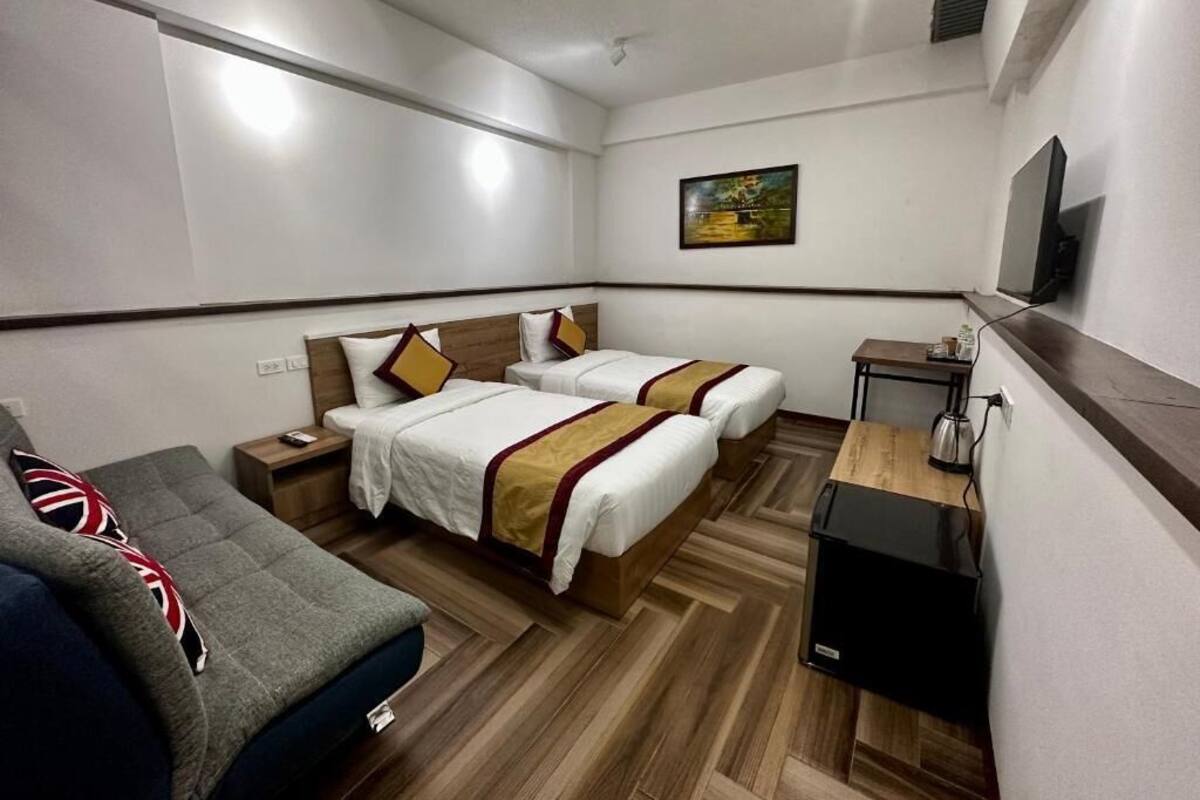 A hotel room with two beds, a sofa, a desk, and a TV.