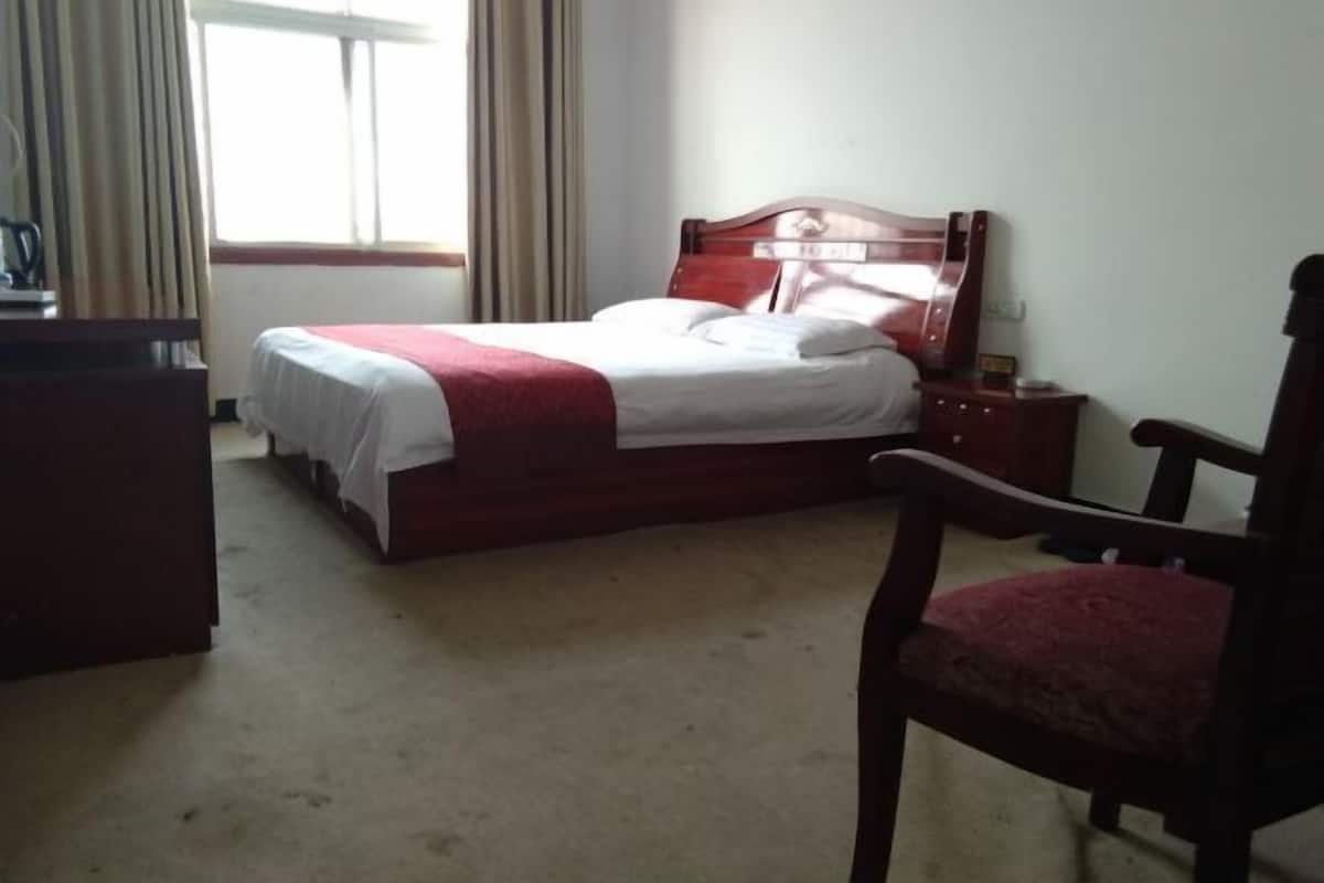 Un dormitorio con cama, una silla, un escritorio y una ventana con cortinas.