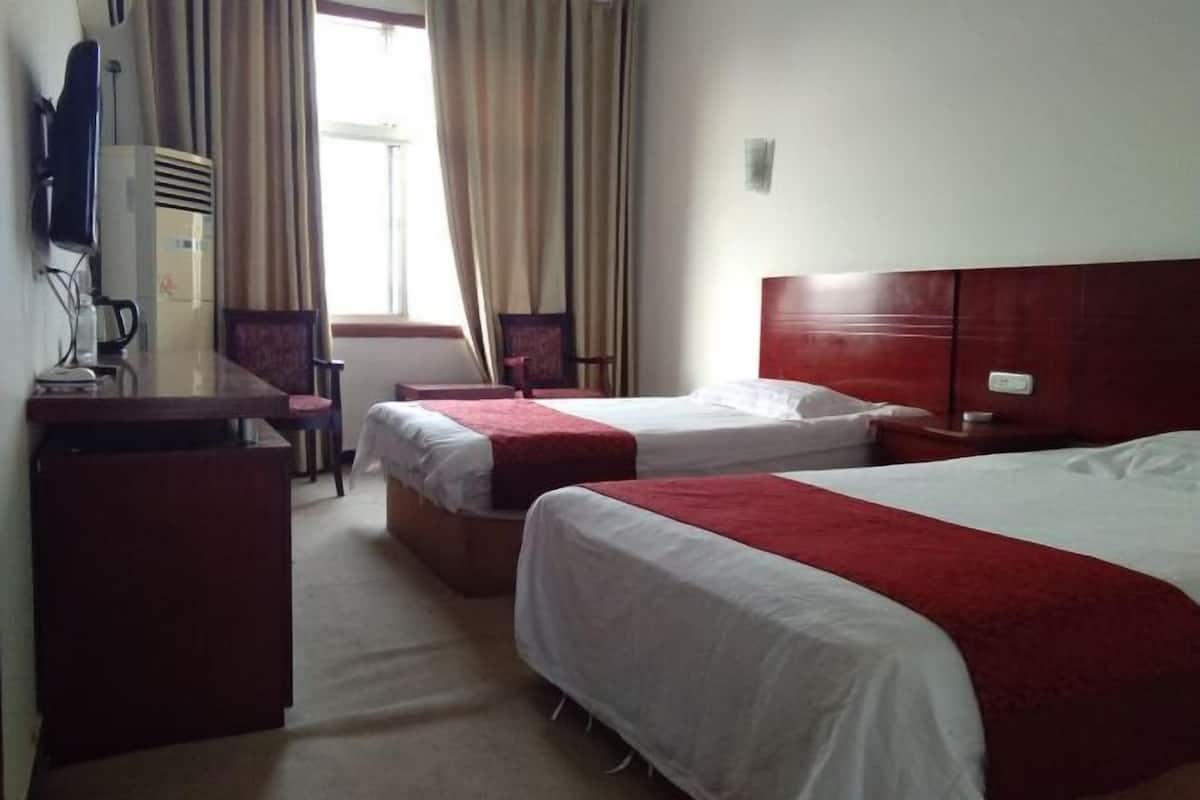 Habitación de hotel con dos camas, un escritorio, una silla, un televisor y una ventana con cortinas.