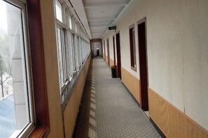 A long corridor with windows on one side and doors on the other, leading to a room at the end.