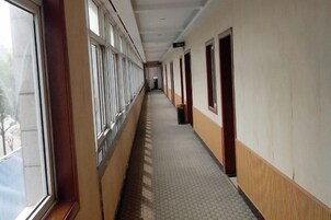 Un largo pasillo con ventanas a un lado y puertas al otro, que conduce a una habitación al final.
