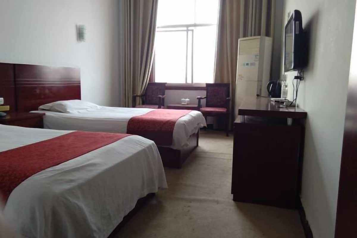Habitación de hotel con dos camas, un escritorio, una silla, un televisor y un ventanal con cortinas.