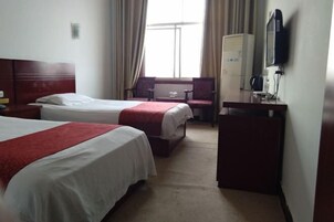 A hotel room with two beds, a desk, a chair, a television, and a window with curtains.