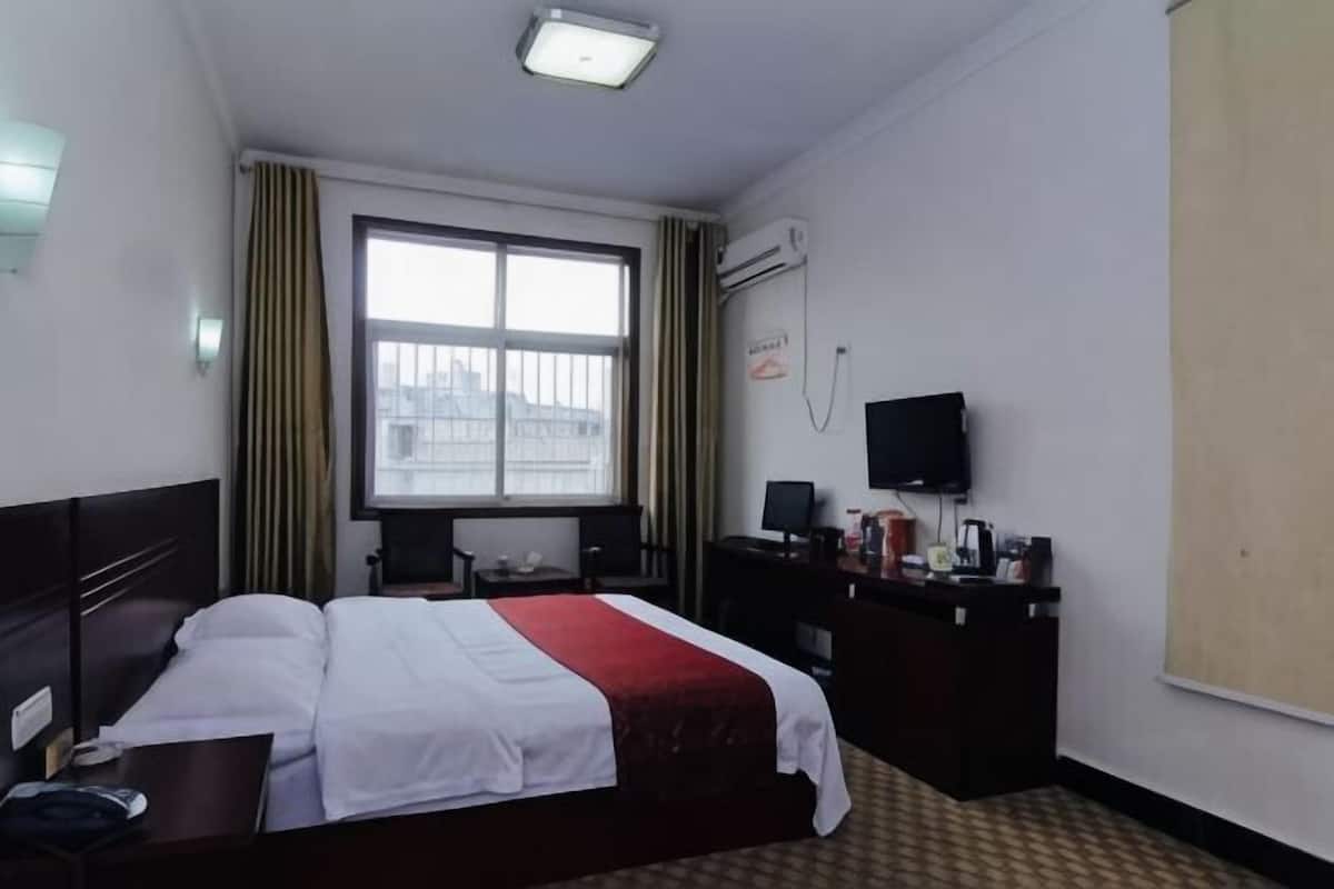 Una habitación de hotel con cama, escritorio, silla, televisor y ventana con cortinas.