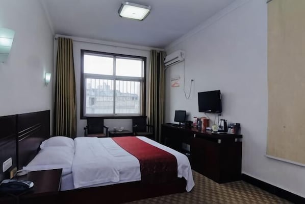Ein Hotelzimmer mit Bett, Schreibtisch, Stuhl, Fernseher und einem Fenster mit Vorhängen.