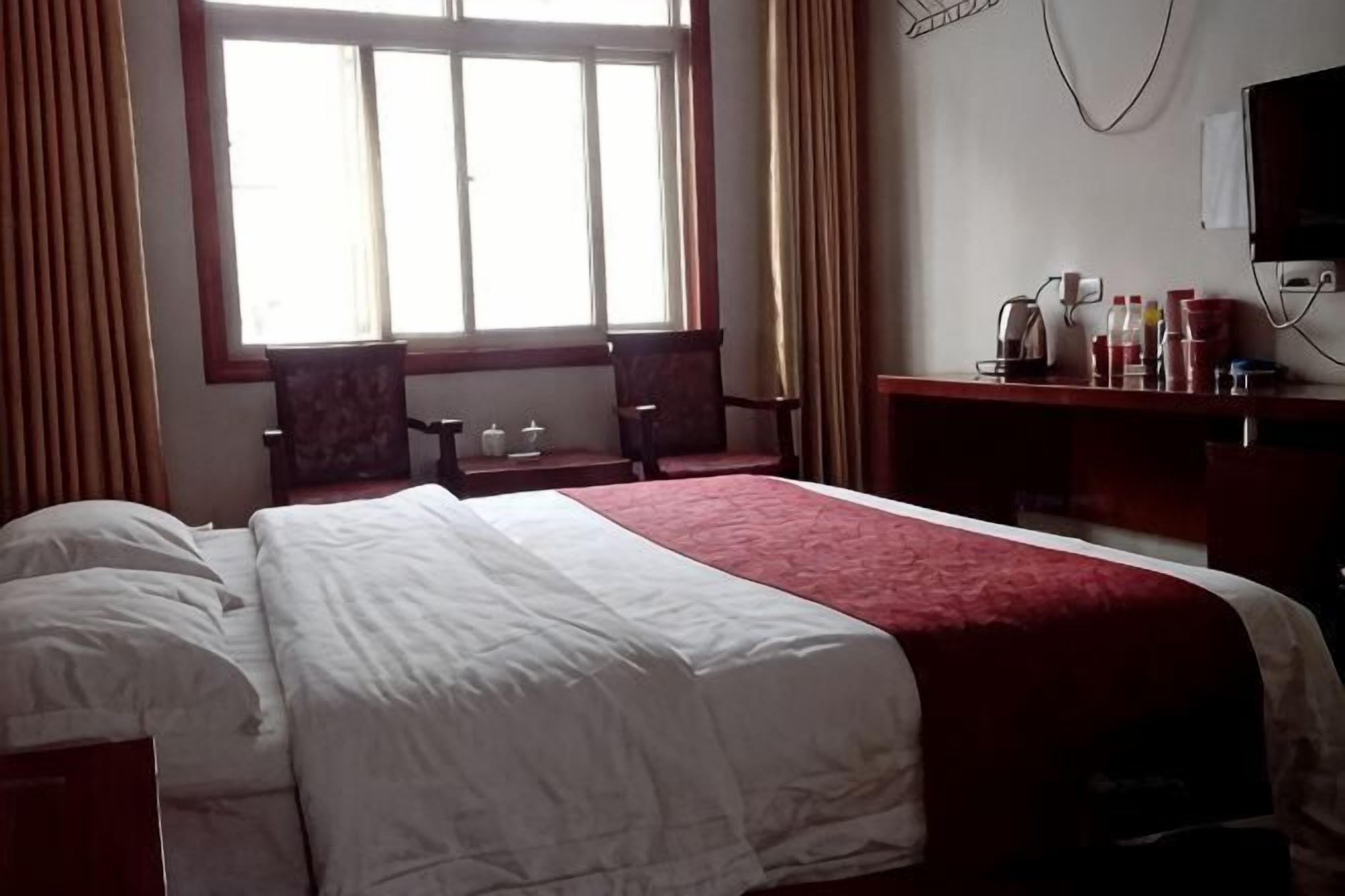 Une chambre d’hôtel avec un grand lit, un bureau avec une chaise, une fenêtre avec des rideaux et un téléviseur fixé au mur.