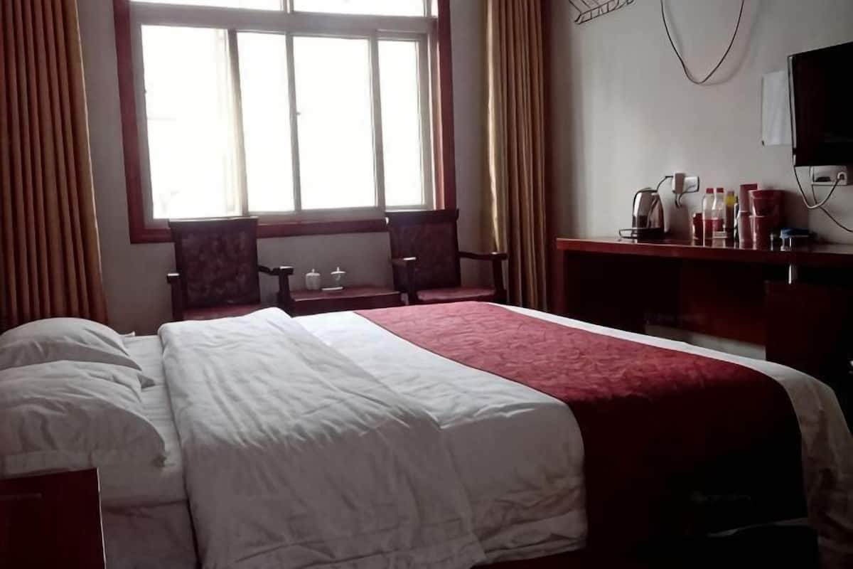 Habitación de hotel con una cama grande, un escritorio con silla, una ventana con cortinas y un televisor en la pared.